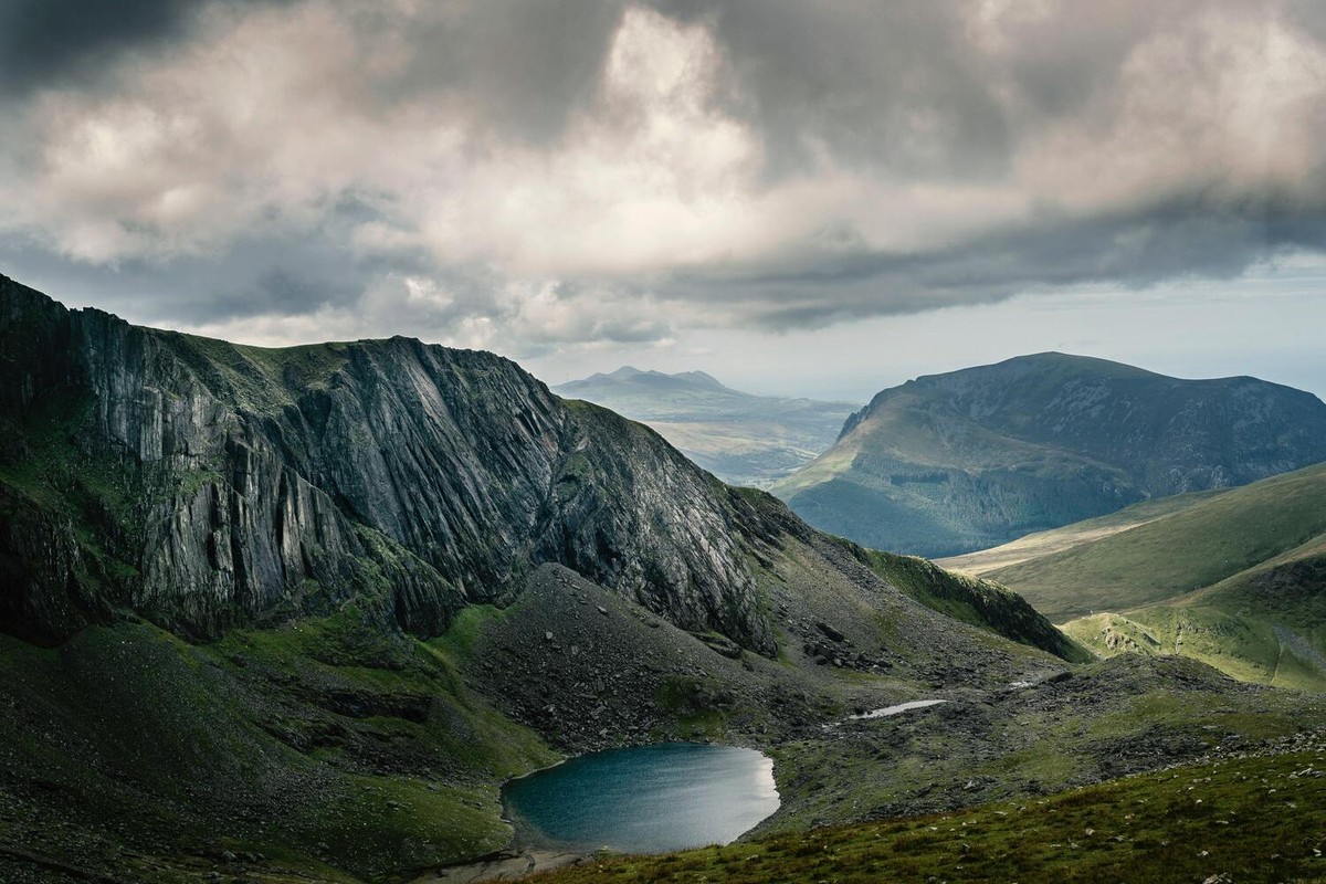 A dramatic mountain landscape with a small lake below rocky peaks.