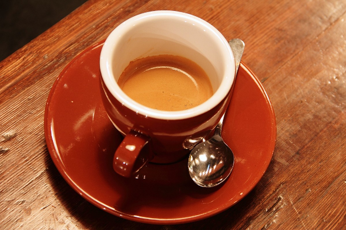 A cup of coffee on a saucer with a spoon on a wooden table.