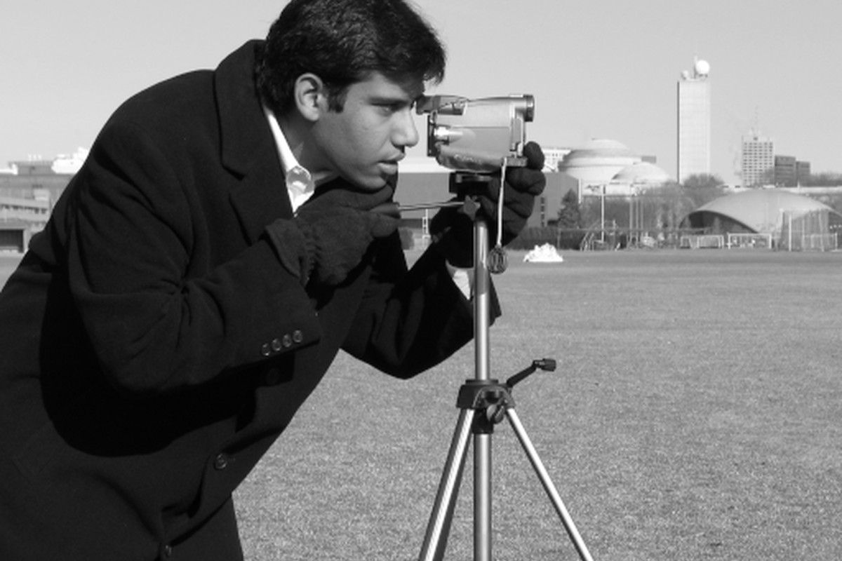 A photographer looking through a camera mounted on a tripod.
