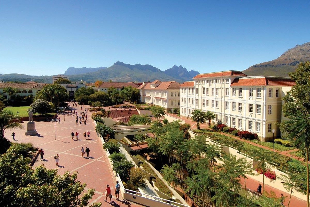 A landscaped university campus with gardens, pathways, and mountains in the distance.